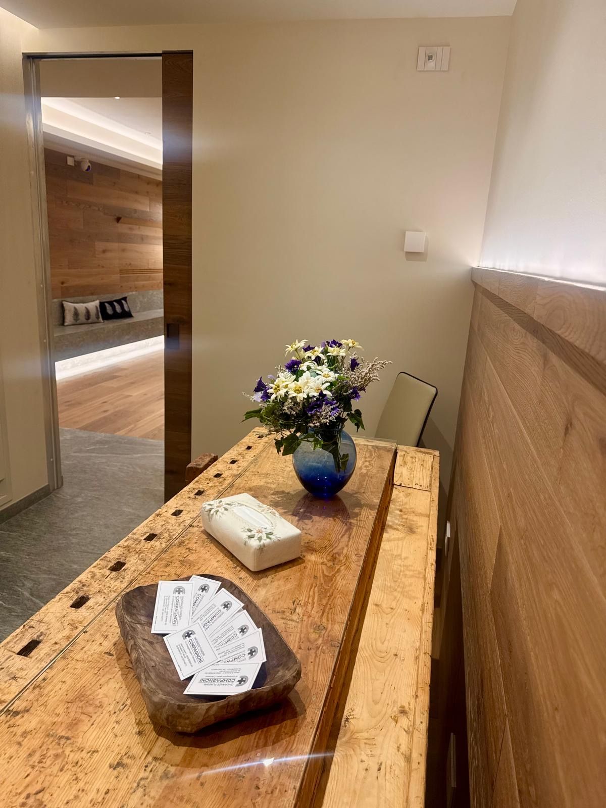 Cucina stretta che si affaccia su un corridoio, con ripiani in legno, plafoniere bianche e una porta blu in fondo.