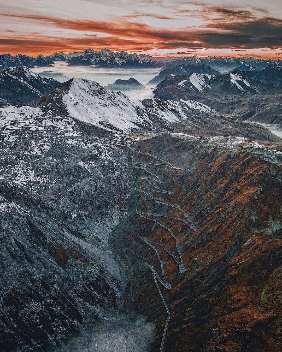 Una vista aerea di una catena montuosa innevata al tramonto.