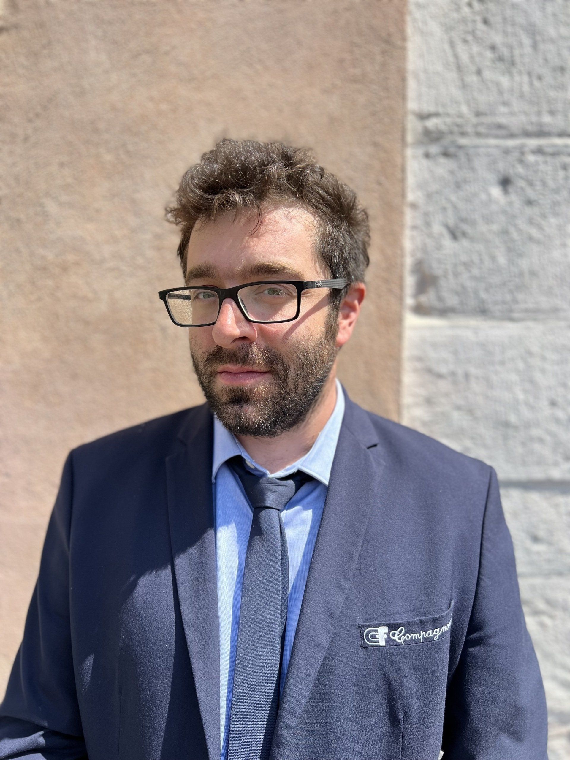 Un uomo in giacca e cravatta è in piedi davanti a un muro.
