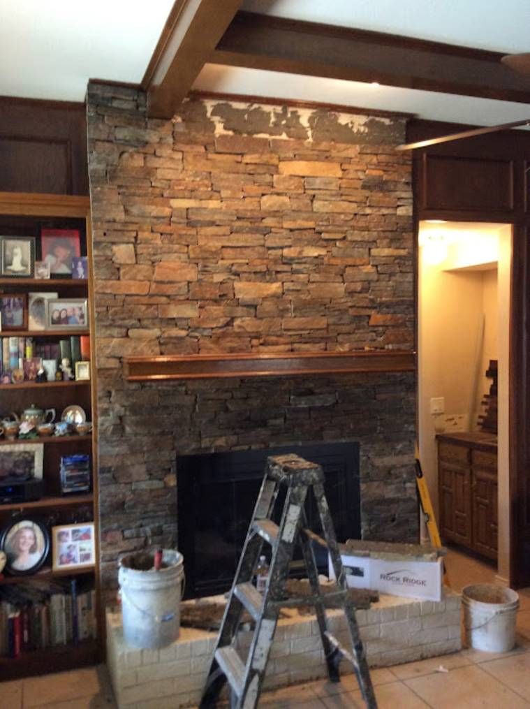 Stone fireplace under construction with ladder, tools, and stacked materials in a wood-beamed room