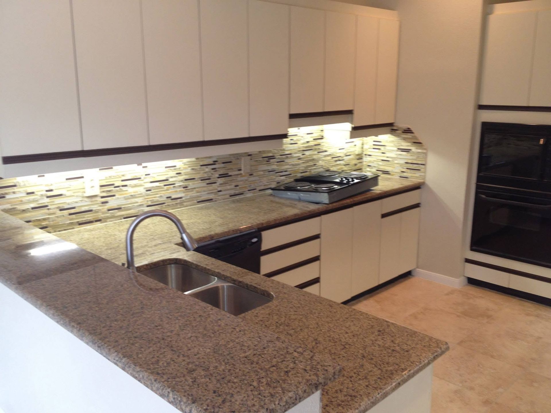 Modern kitchen with beige cabinets, granite island, sink, stove, and mosaic tile backsplash