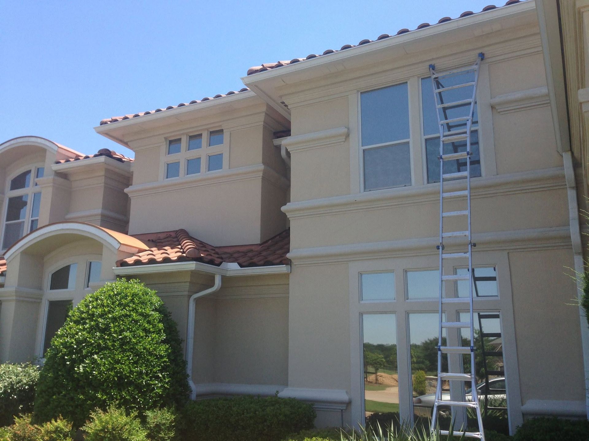 Two-story beige house with large windows and a ladder leaning against the right side.