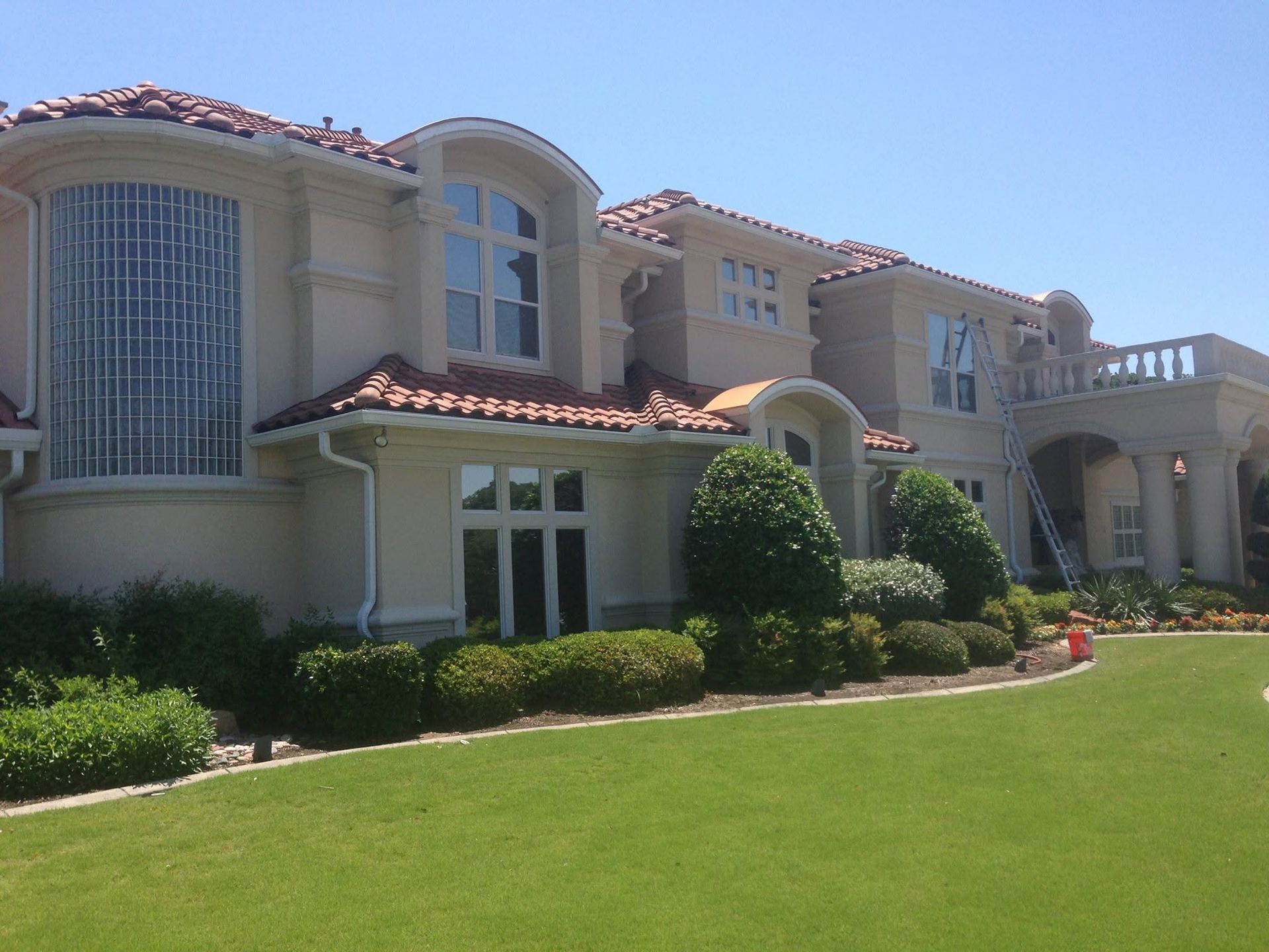 Large cream-colored Mediterranean-style house with red tile roof and manicured green lawn under a blue sky
