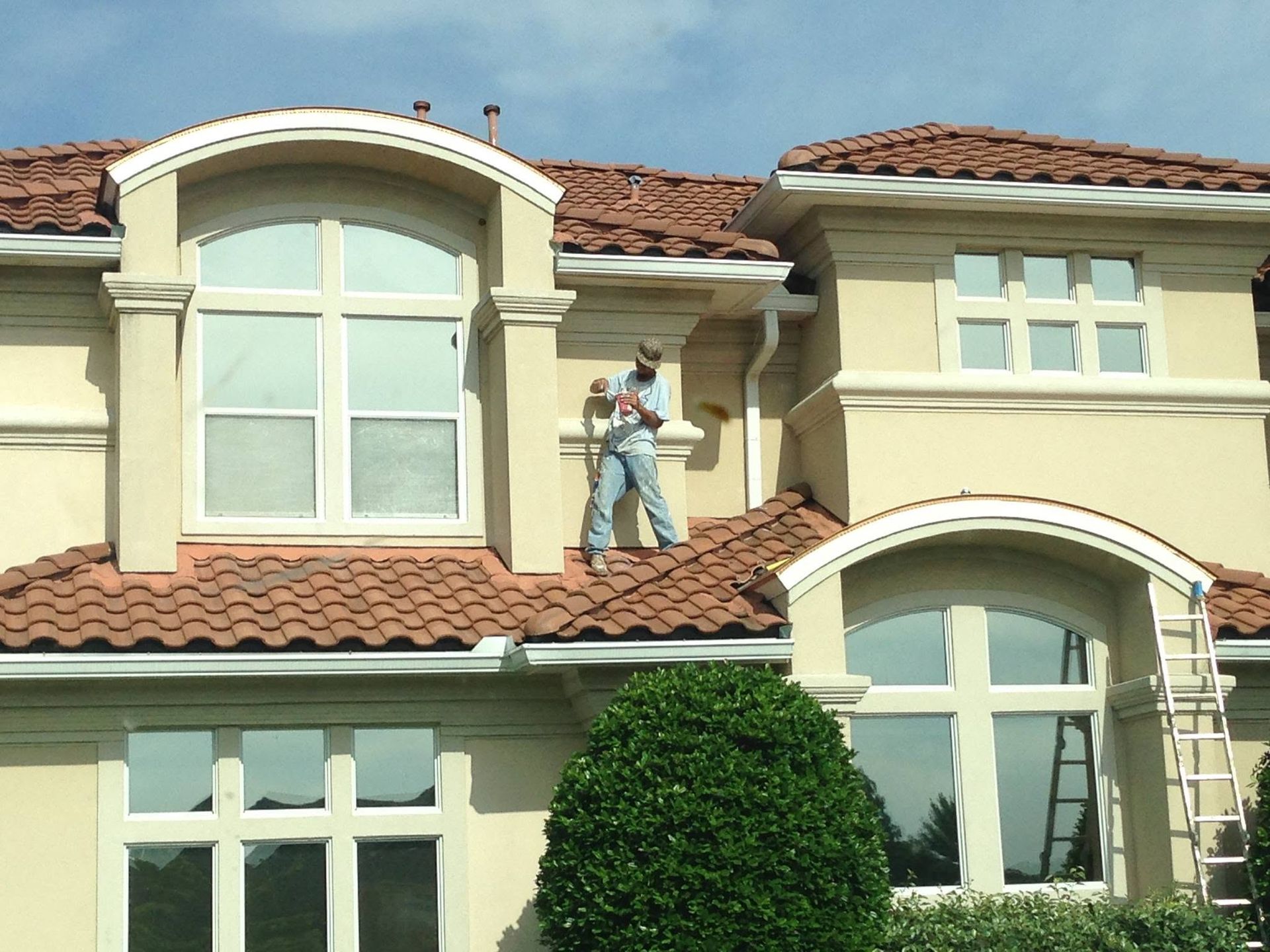 Roofers working on a beige stucco house with a tiled roof and large arched windows
