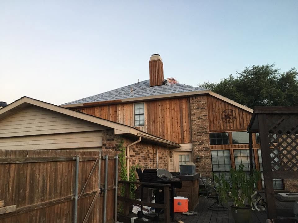 Backyard with wooden sheds, a brick house, and a black grill under a clear sky