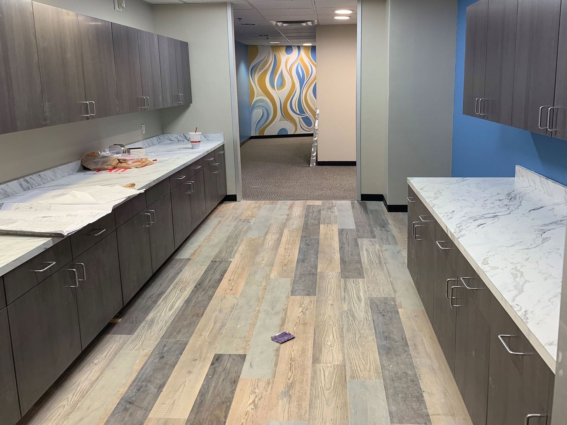 Modern kitchen with gray cabinets, white countertops, blue accent wall, and patterned rug runner