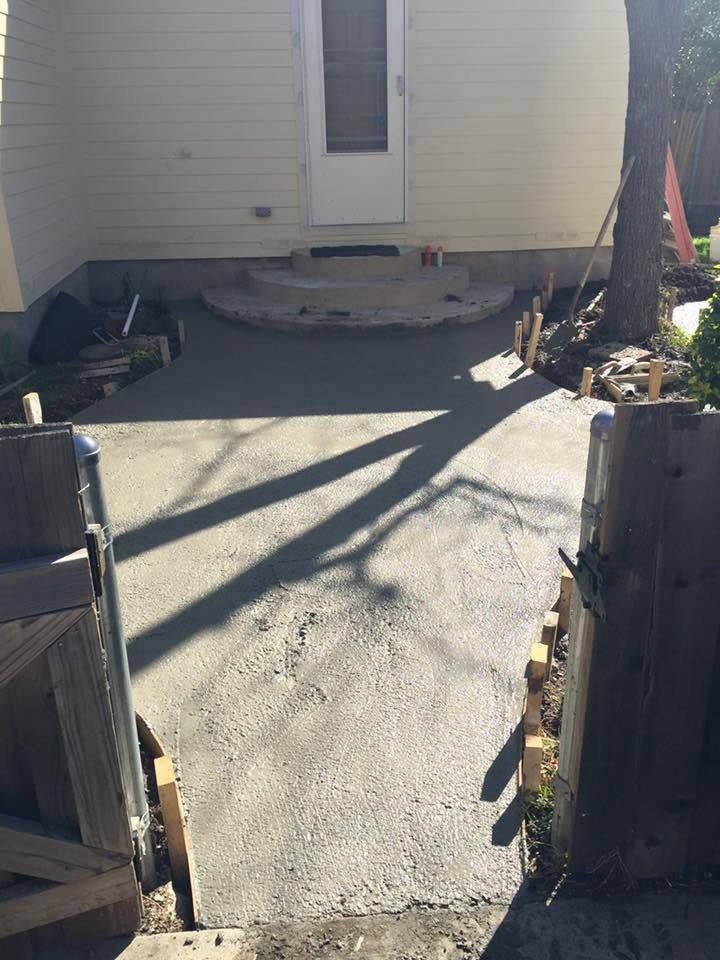 Concrete patio leading to a white door, framed by wooden fence posts and long shadows.