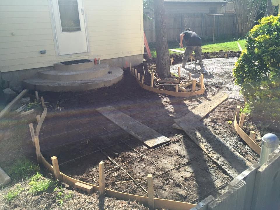 Worker laying wood forms for a patio beside a house in a dirt yard