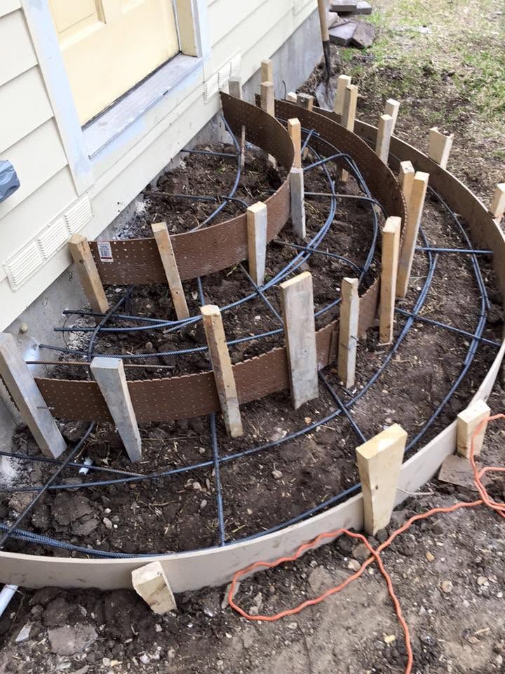 Curved tiered garden bed with wooden edging and irrigation tubing beside a house