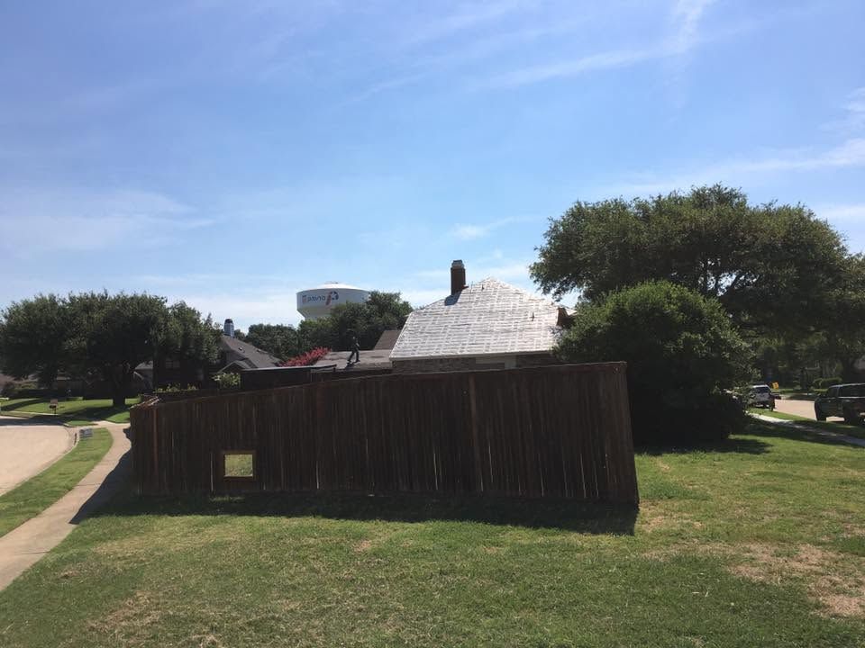 Small rustic cabin with a dark wooden fence in a sunny grassy park.