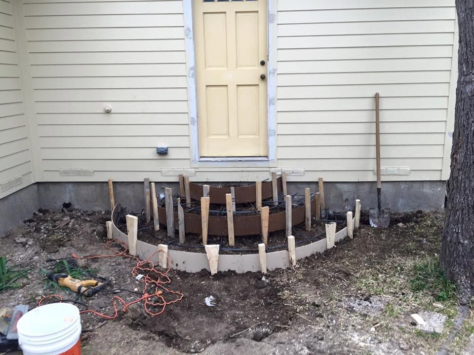 House exterior with a small curved retaining wall under construction beside a cream-colored door