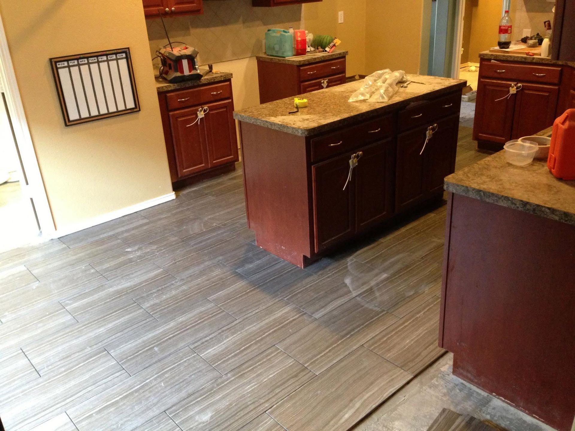 Empty kitchen with dark wood cabinets, granite island, and gray wood-look flooring.