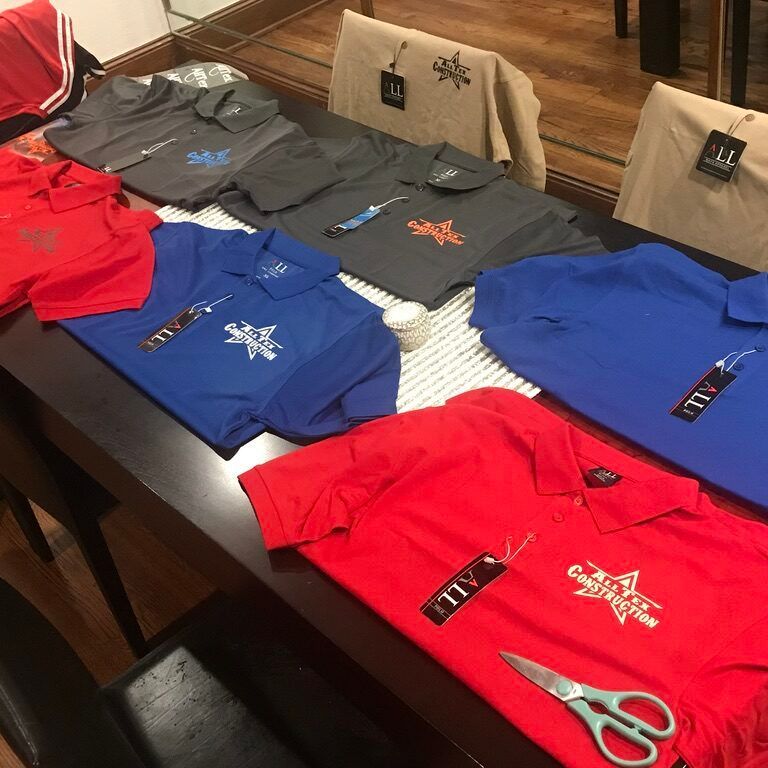 T-shirts in red, blue, gray, and beige laid out on a table with scissors nearby in a retail setting