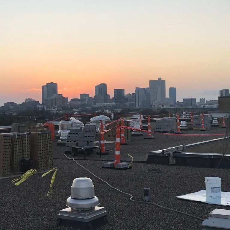 Rooftop at sunset with city skyline and scattered construction materials and safety cones