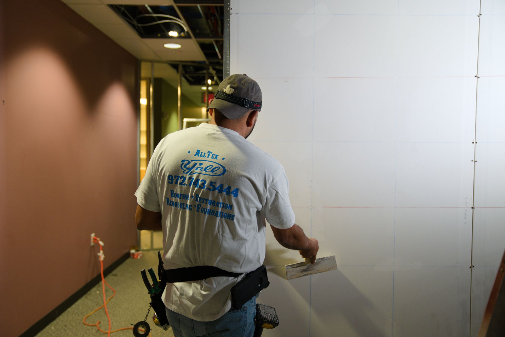 Worker in hard hat sanding a wall in a hallway under construction