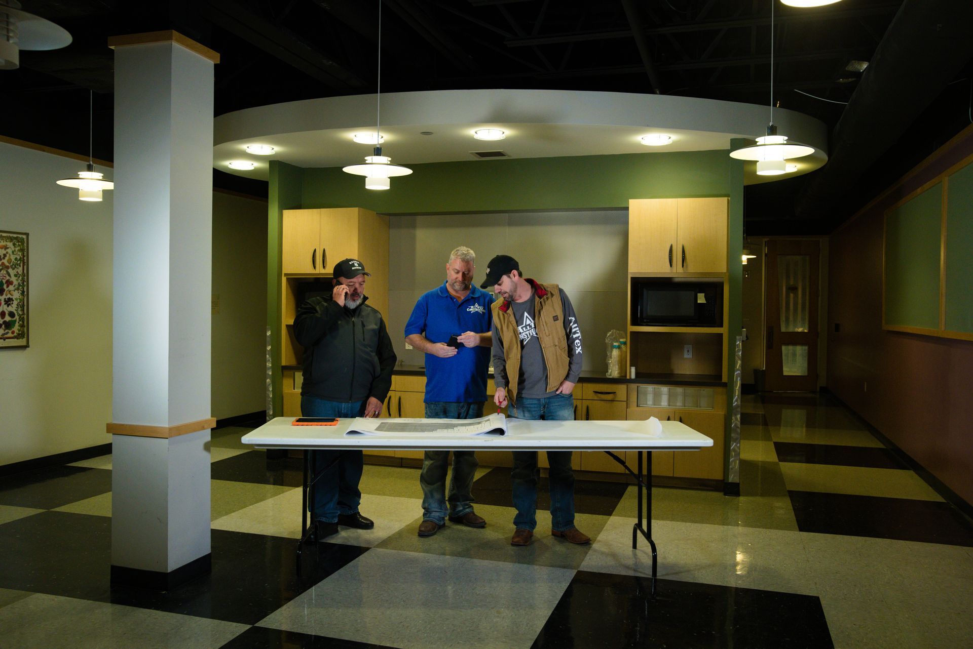 Three people standing behind a table in a brightly lit lobby or community hall