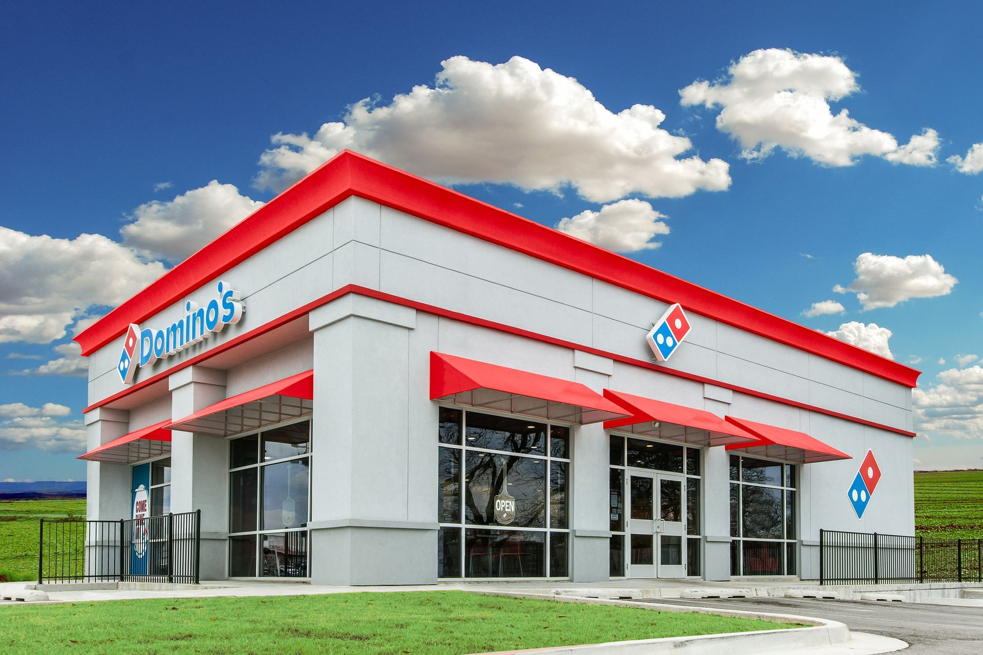 Modern white-and-red Domino’s pizza restaurant with glass entrance under a blue sky