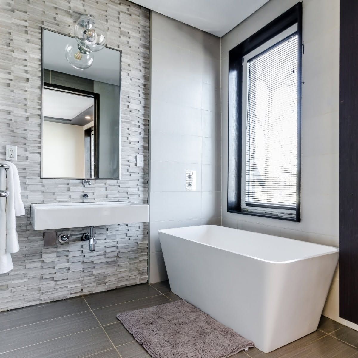 Modern bathroom with white vanity, large mirror, freestanding tub, and window blinds