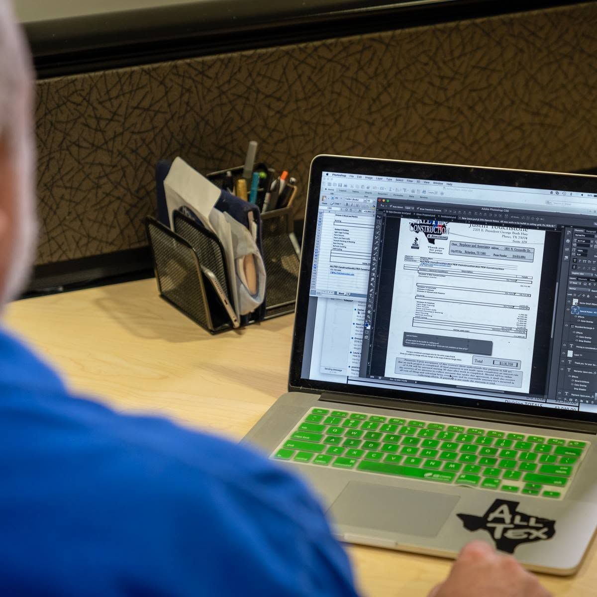 Person at a desk using a laptop with a bright green keyboard in an office cubicle.