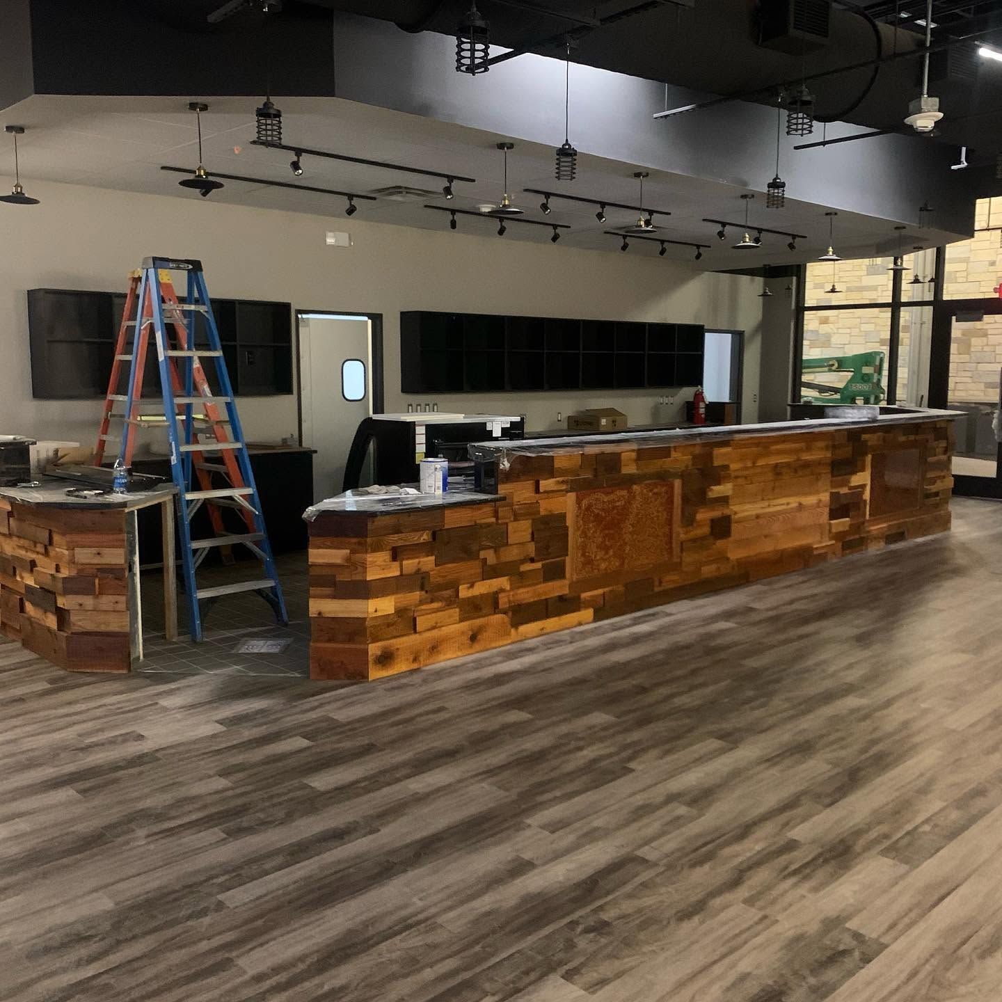 Modern office reception area with wood front desk, blue ladder, large screens, and empty flooring