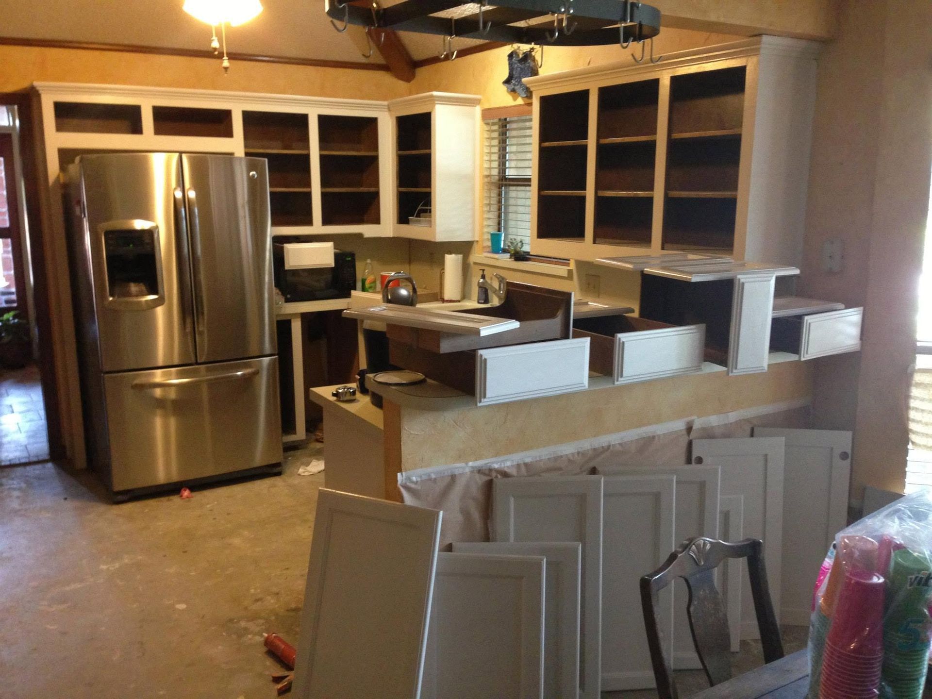 Unfinished kitchen with stainless refrigerator, wood cabinets, and stacked cabinet doors in the foreground