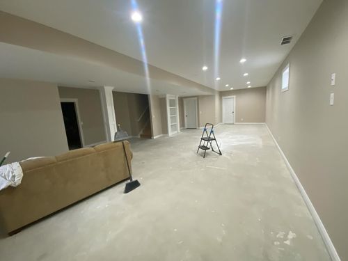 Empty unfinished basement with beige walls, recessed lights, ladder, and a couch in the foreground