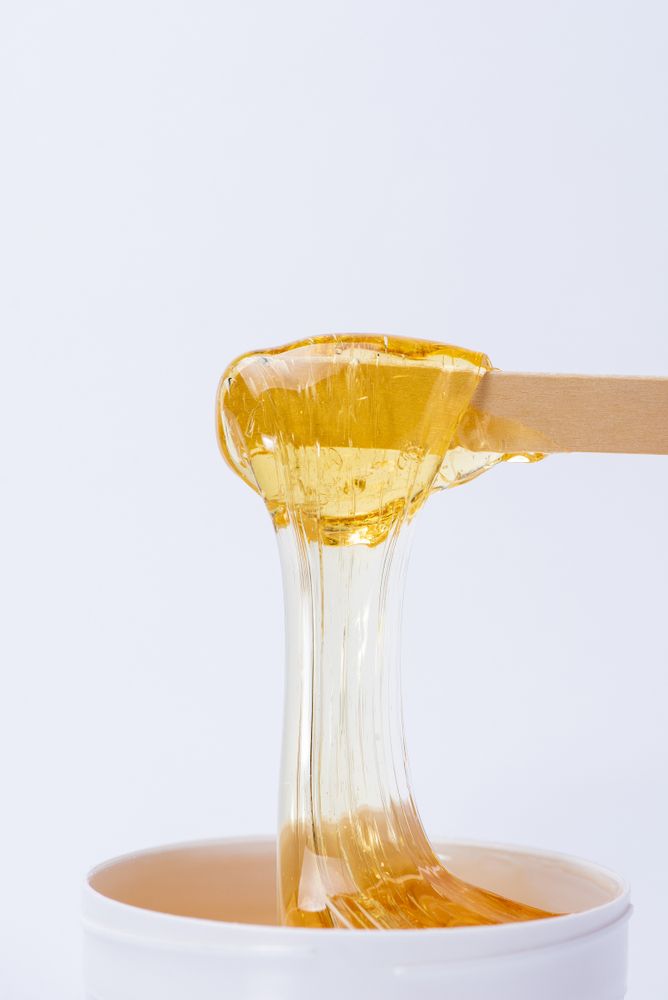 Wax Applicator Dripping Honey-Colored Wax Into a White Container — Beauty In Profile In Salamander Bay, NSW