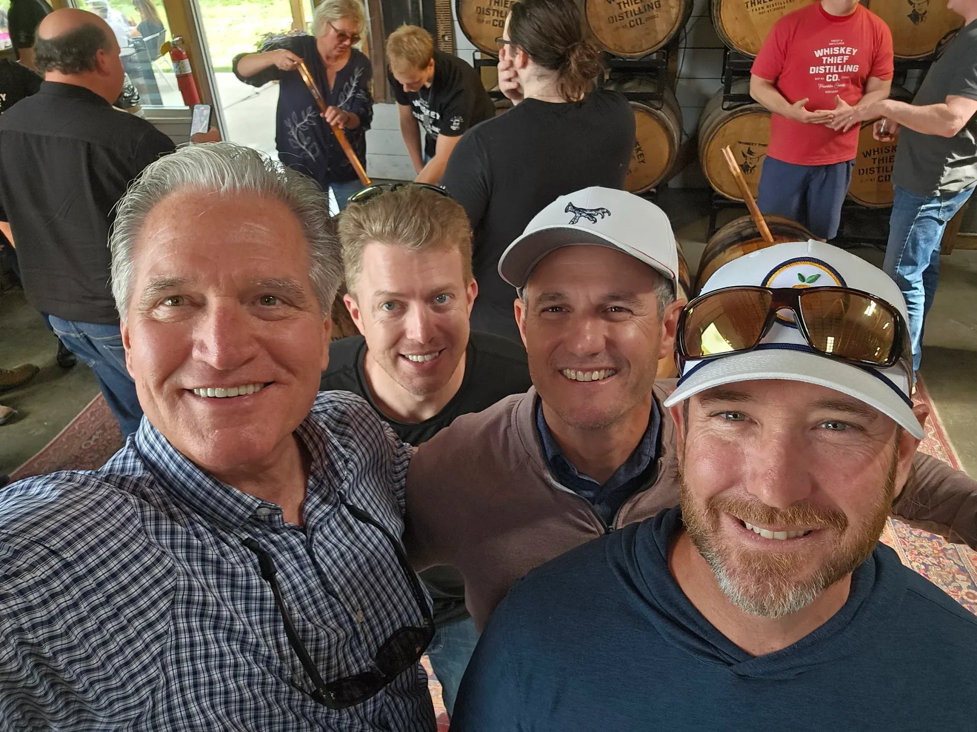 Four smiling friends posing for a selfie in a busy indoor gathering space