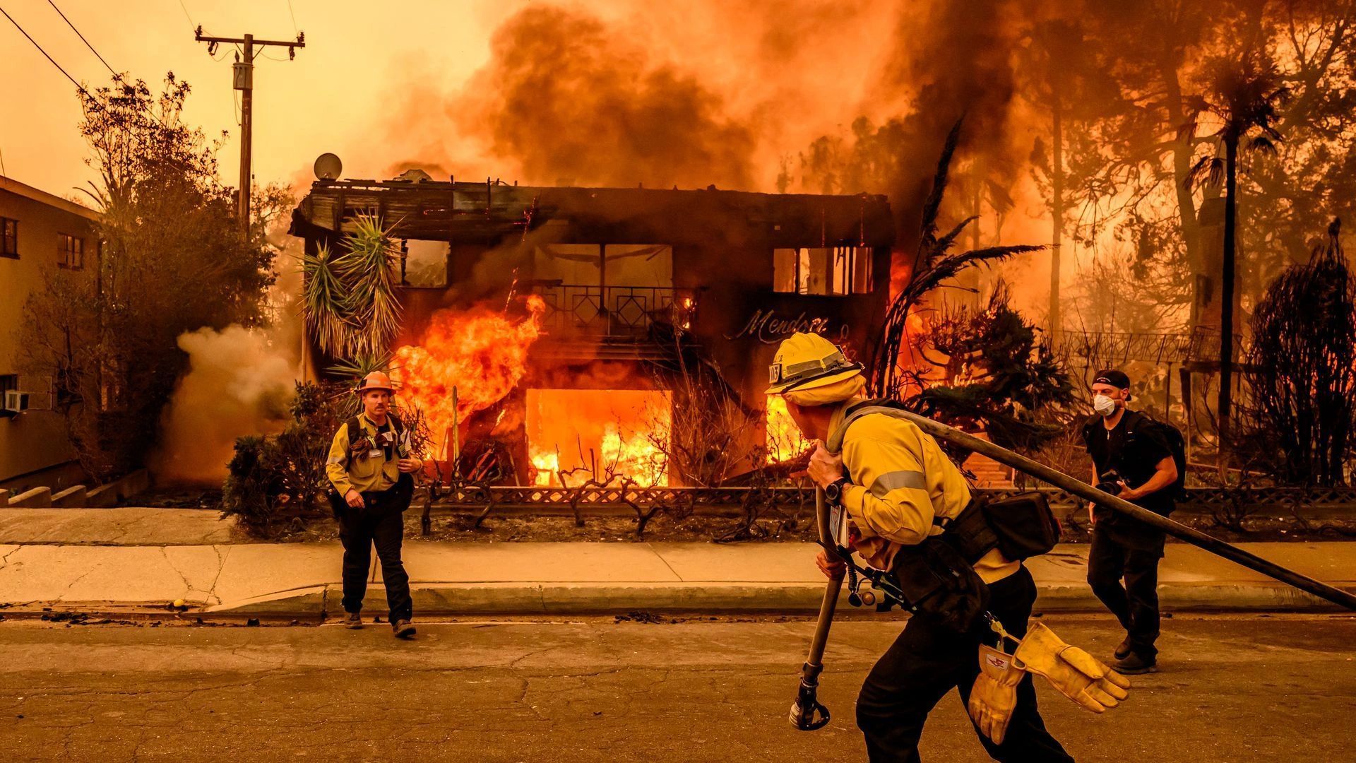 Firefighters battle a burning house amid thick smoke and flames.
