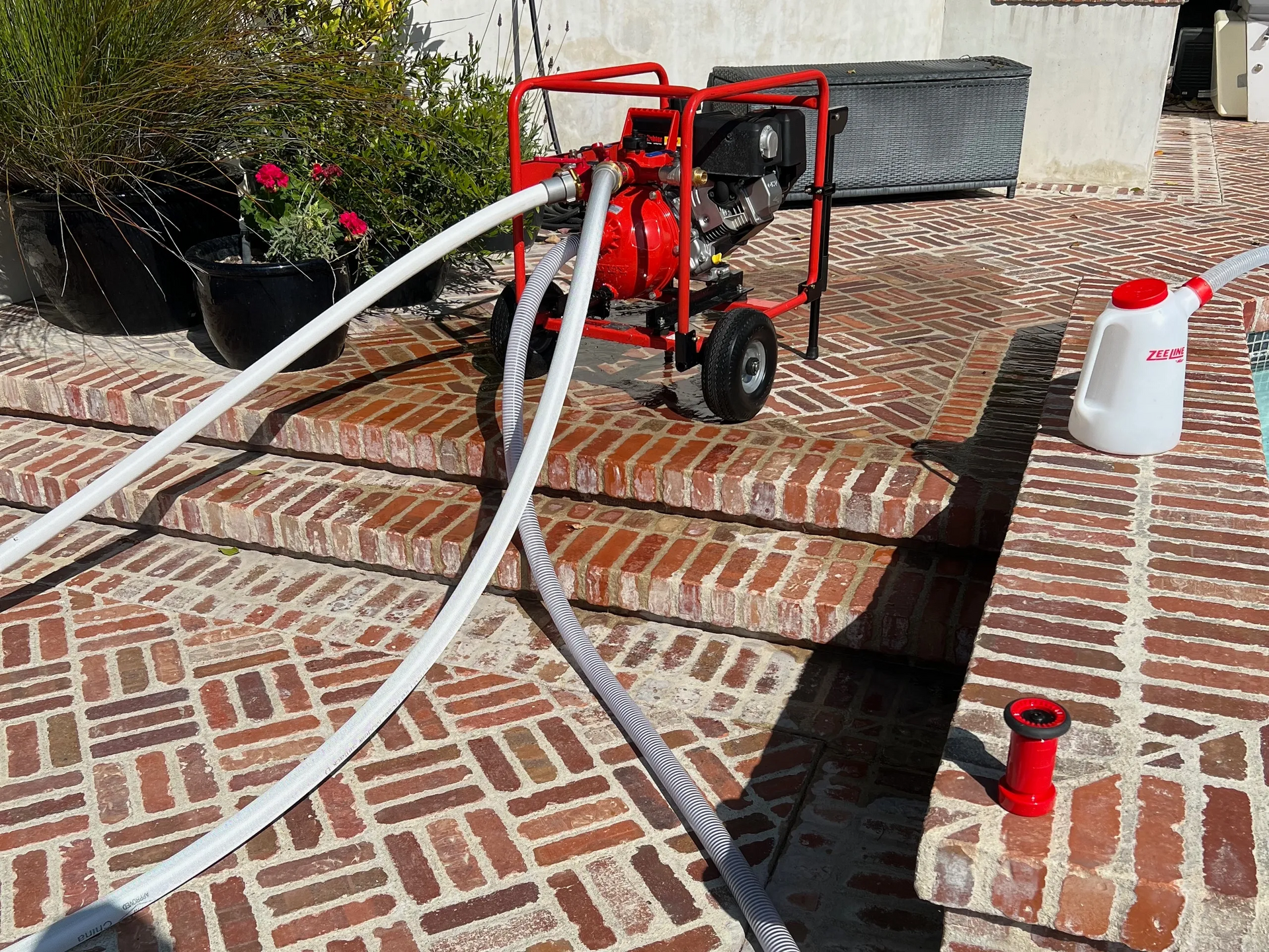 Red water pump with hoses on brick steps and pool deck.