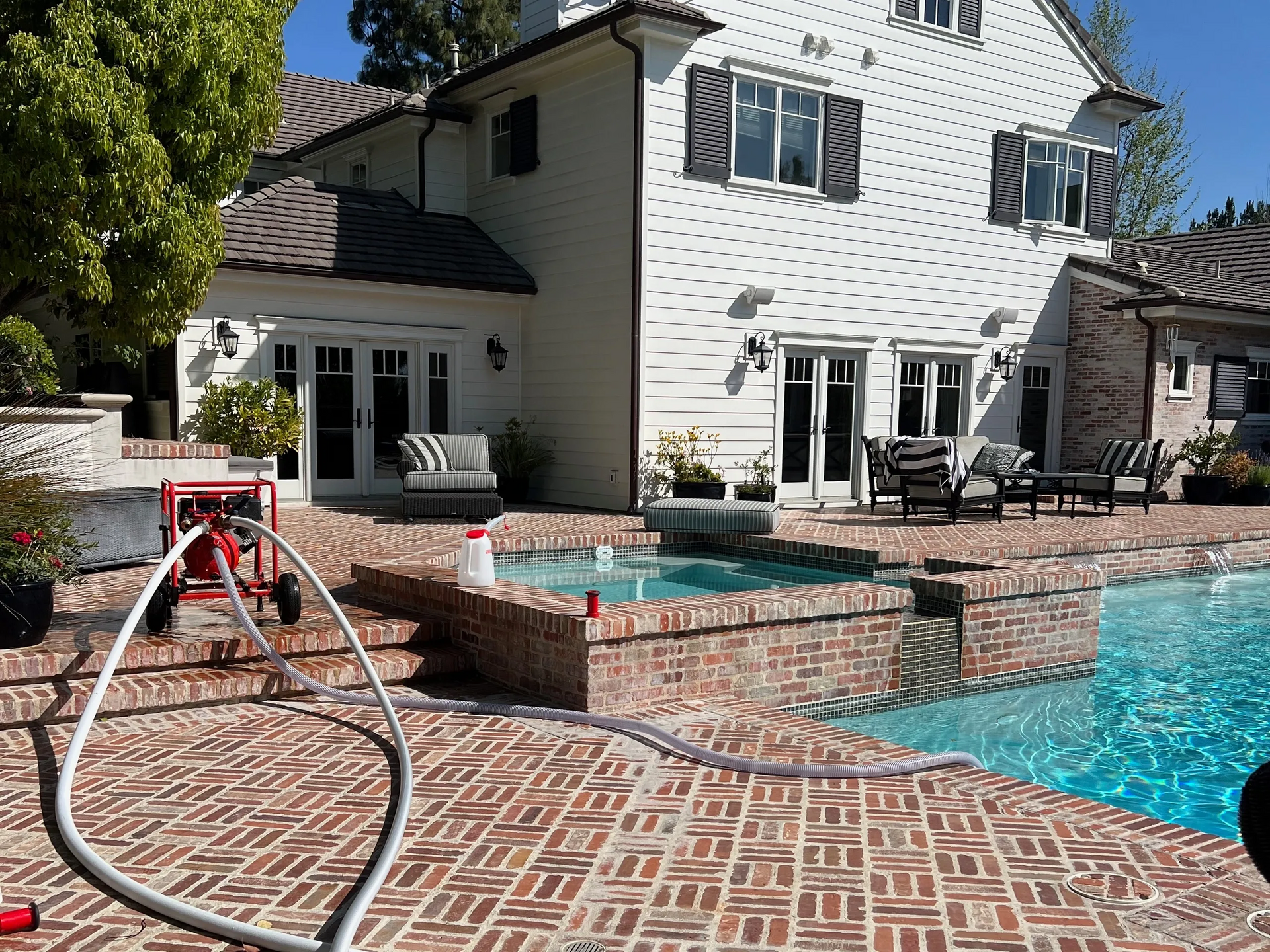 Brick patio and pool next to a white house with black shutters. A red pump is visible.