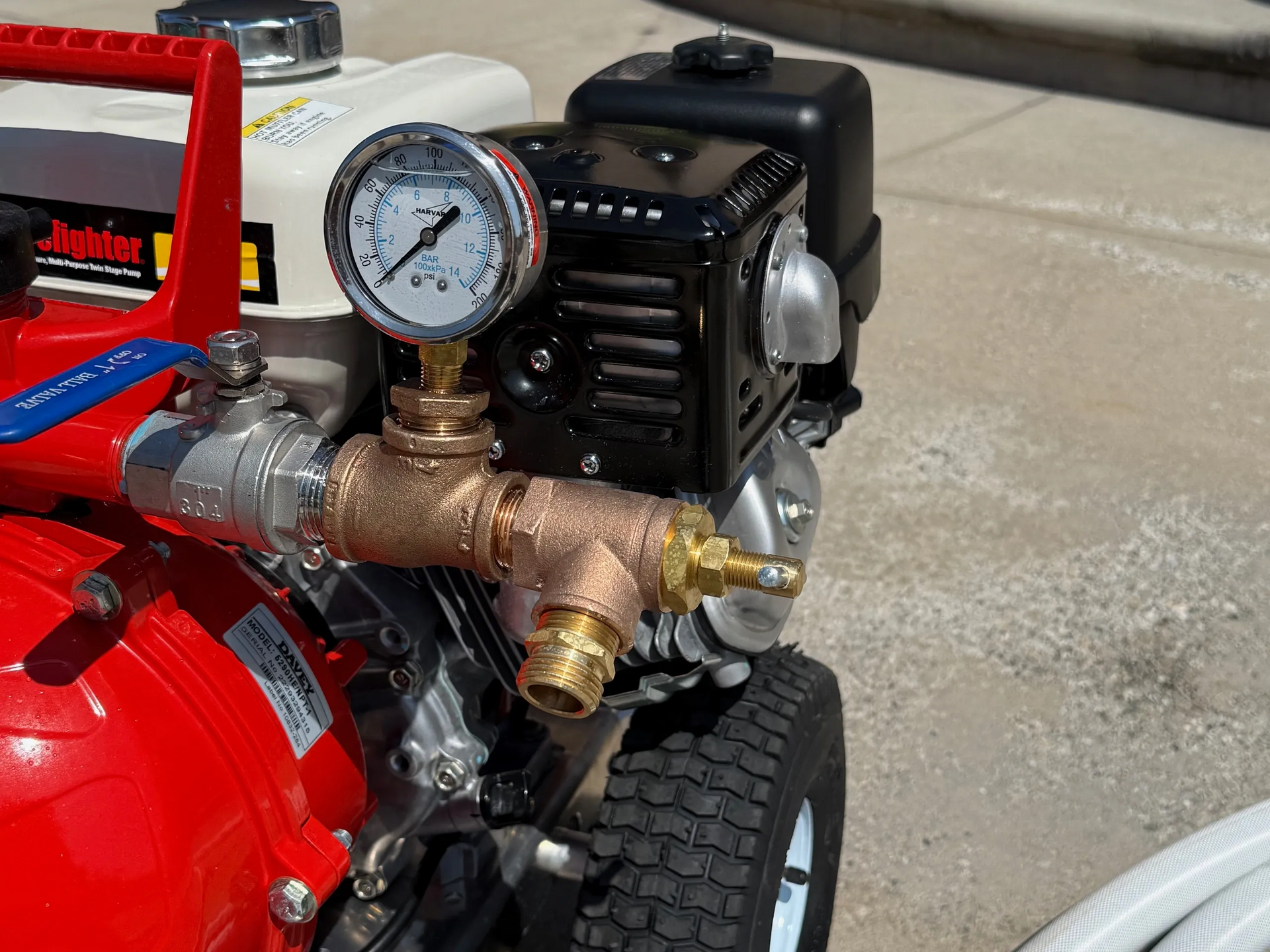 Close-up of a pressure gauge and valves on a red and black motorized pump, possibly for water.