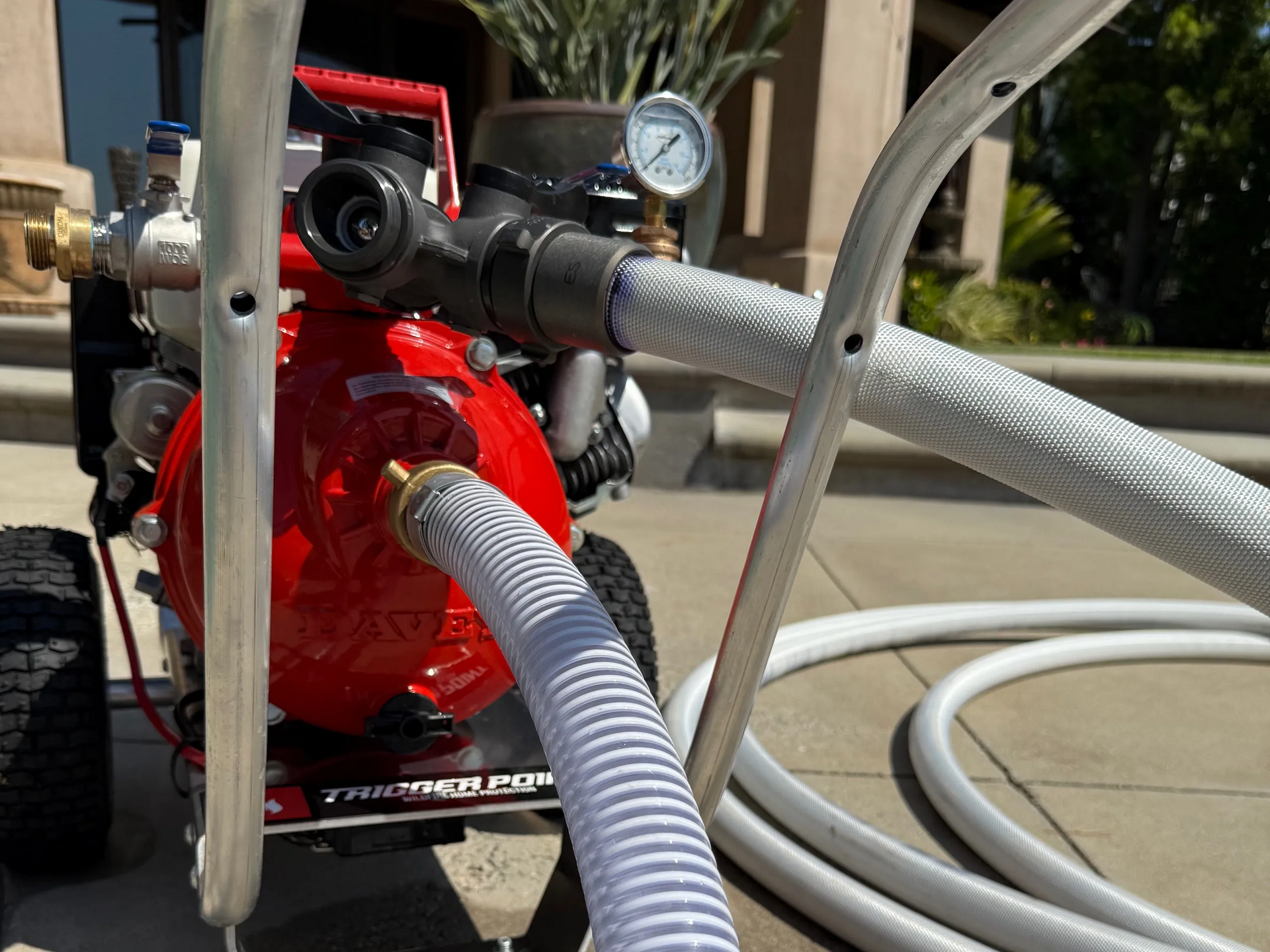 Red and silver paint sprayer with hoses and a pressure gauge, outdoors.
