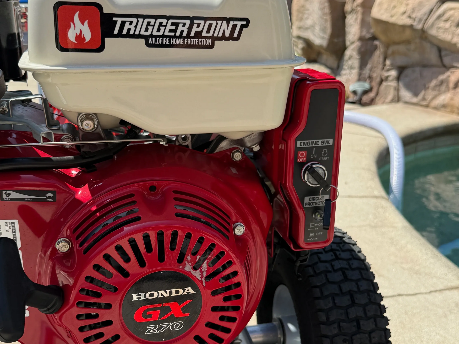 Red Honda GX270 engine with Trigger Point details, mounted on a pressure washer with a pool in the background.