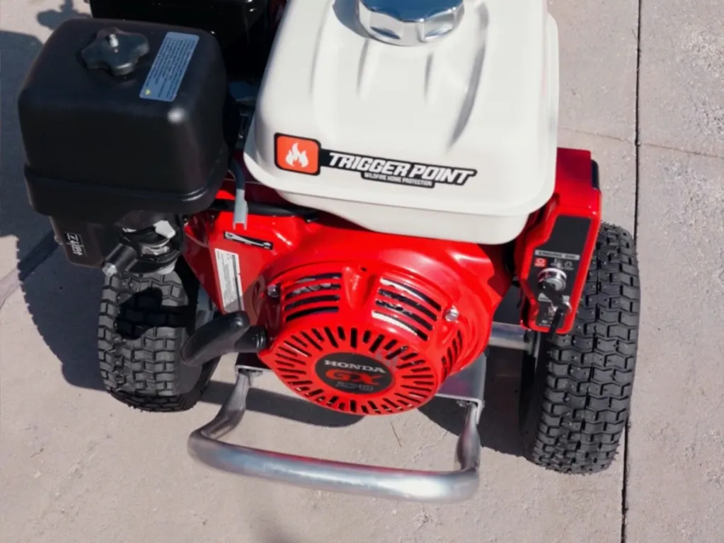 Red and white power washer with black components and small tires, outdoors on concrete.