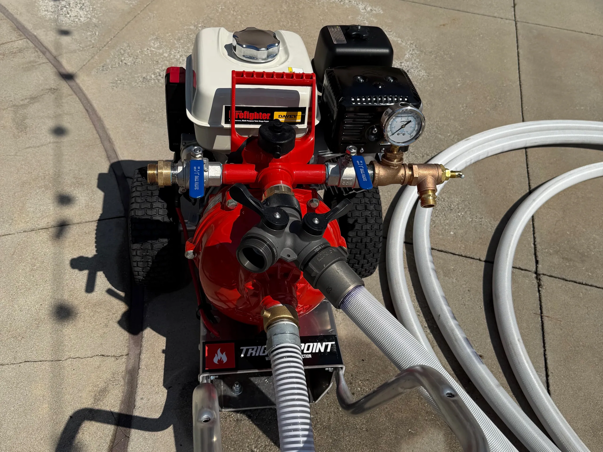 Gas-powered water pump on wheels with hoses, on a concrete surface, for water transfer.