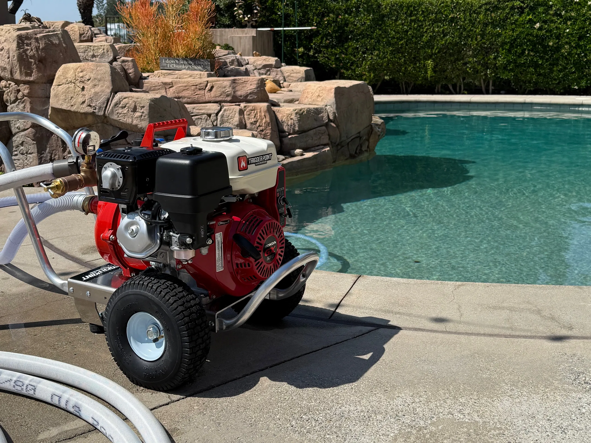 A red engine on a wheeled frame next to a pool. Hoses connect to the engine.