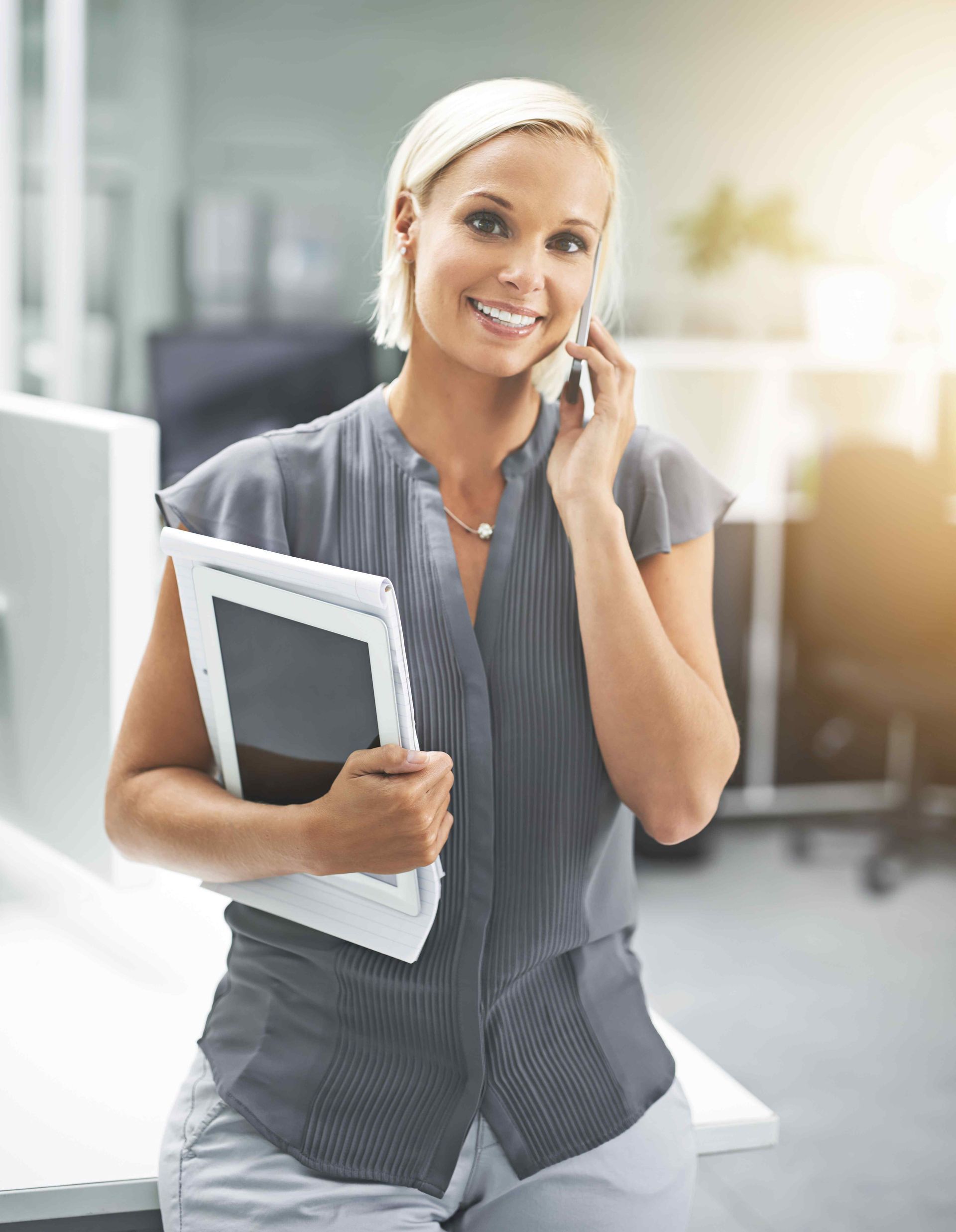A woman is holding a tablet and talking on a cell phone.