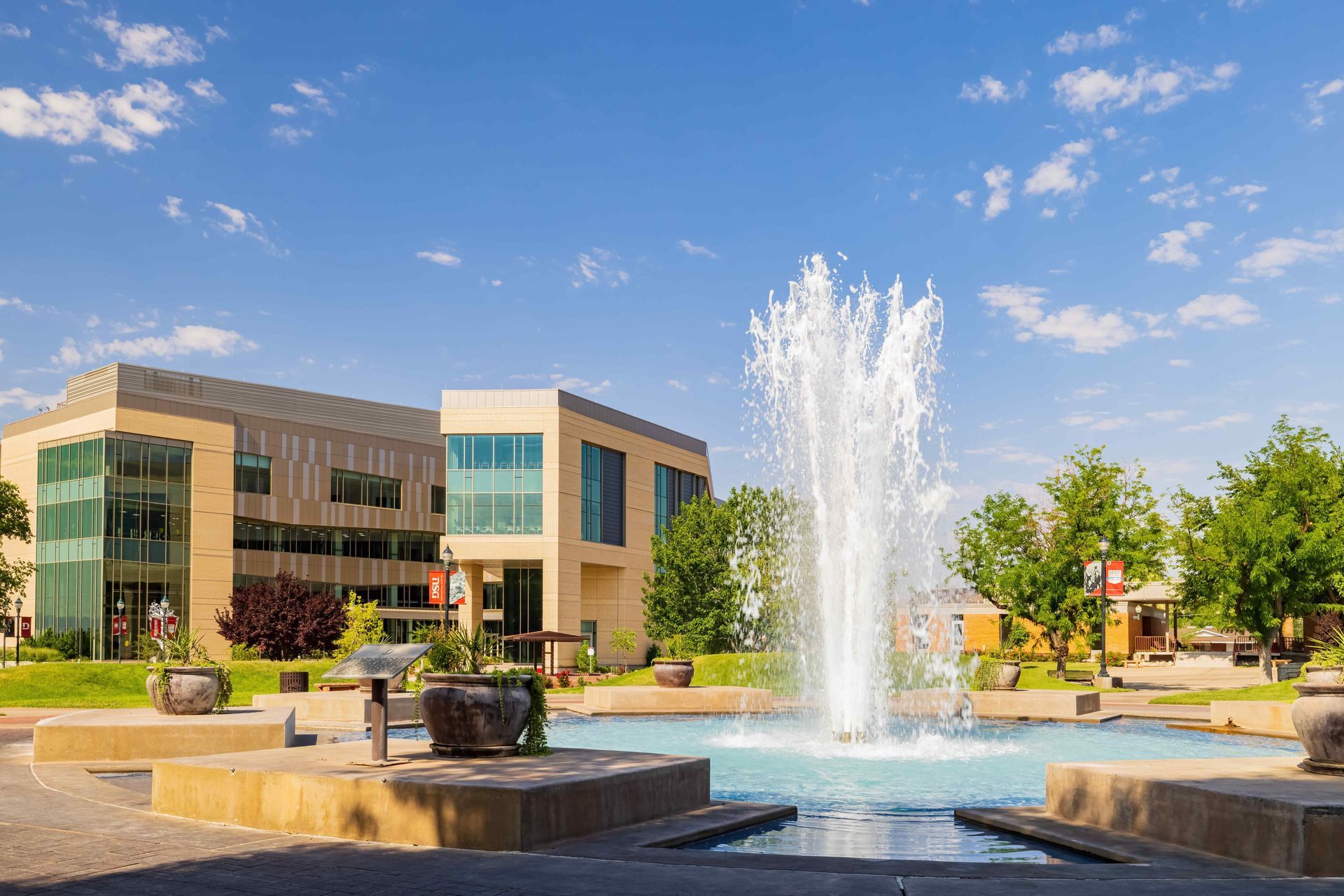 A large building, Dixie State University, with a fountain in front of it.