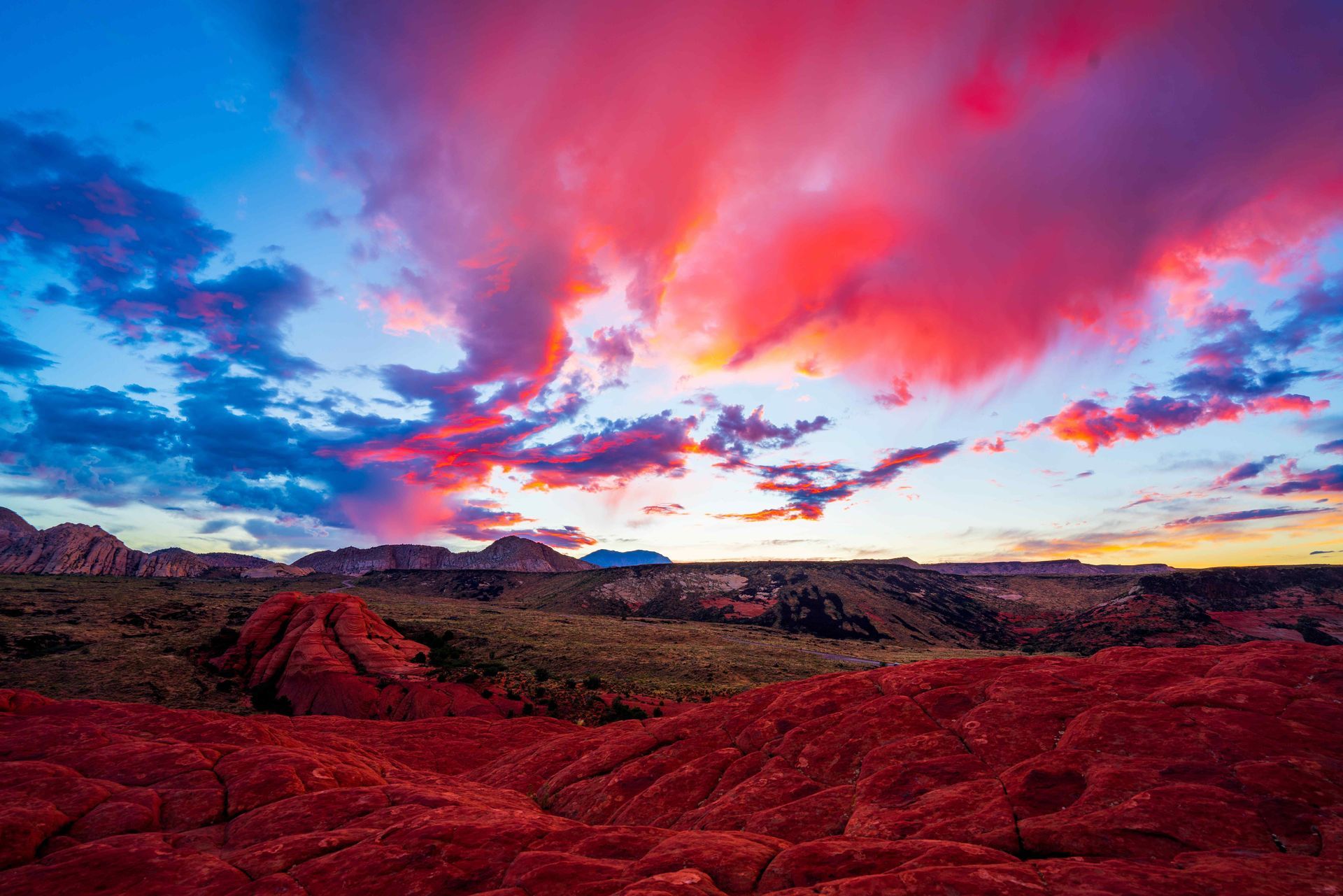 A colorful sunset over a desert landscape, in St. George Utah, with mountains in the background.