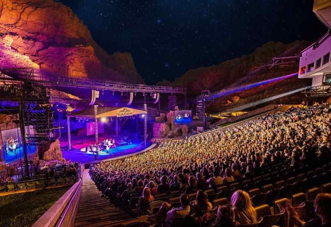 A large crowd of people are sitting in an amphitheater watching a concert in St. George Utah.