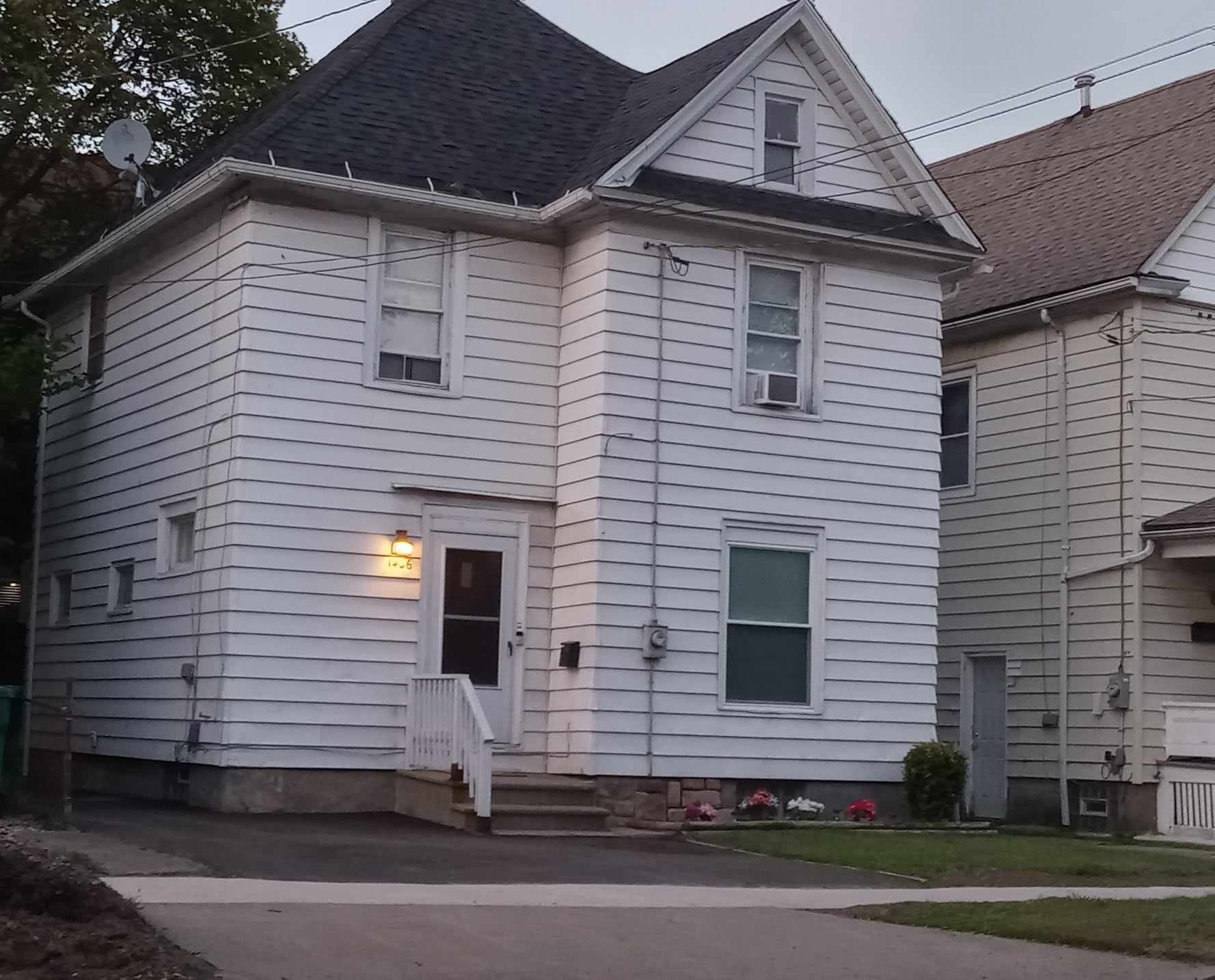 White two-story house with a dark roof, siding, and small front porch, next to a similar house.