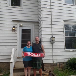 Couple standing in front of a house, holding a 