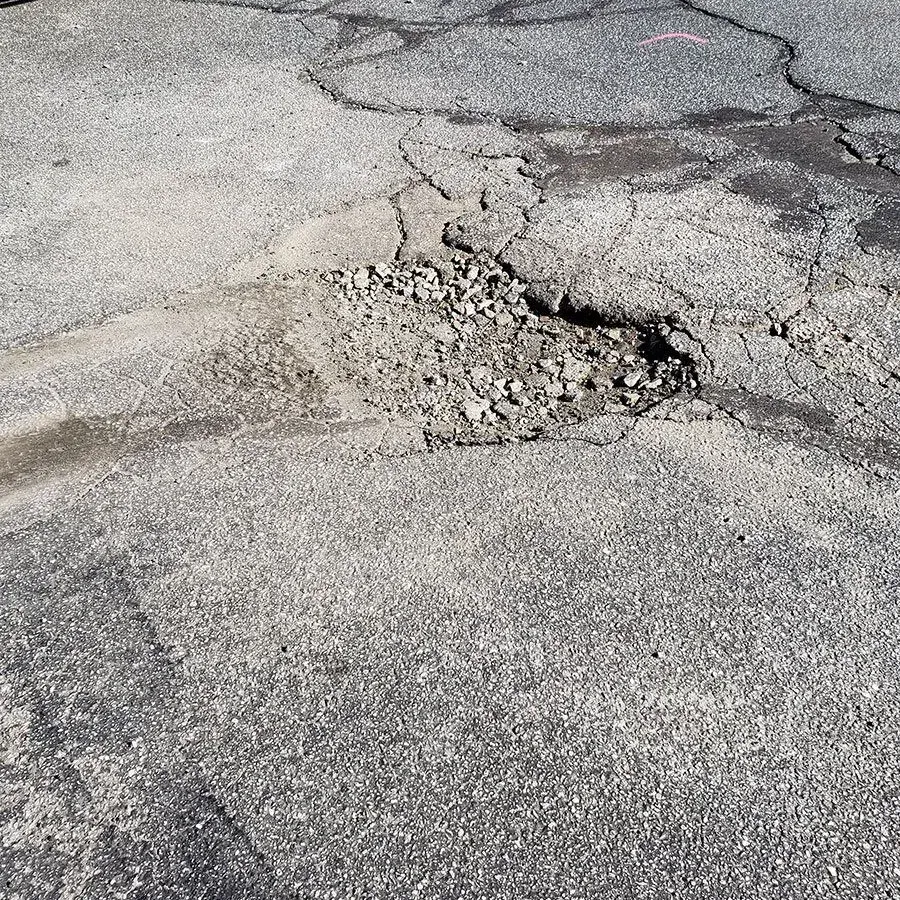 A close up of a cracked asphalt road with a hole in it.