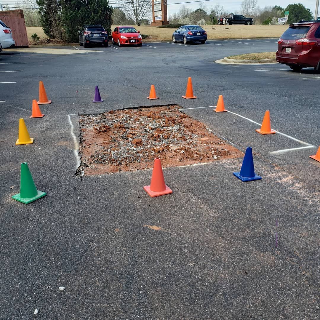 A hole in the ground is surrounded by traffic cones in a parking lot