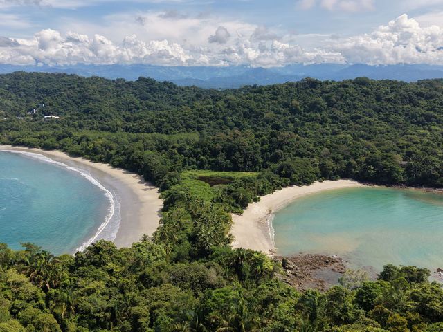 Aerial view of a lush tropical coastline with two crescent beaches and turquoise water of Manuel Antonio National park