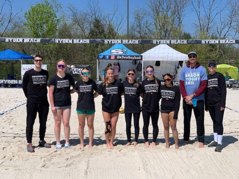 Beach volleyball team, black shirts, posing on sand. 