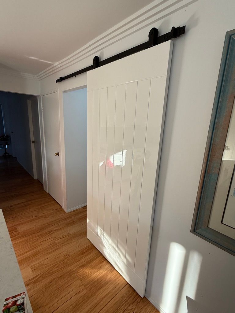 White Barn Door on Black Track in A Sunlit Hallway with Wood Floors and A Wall Mirror — JPR Concepts in Burleigh Heads, QLD