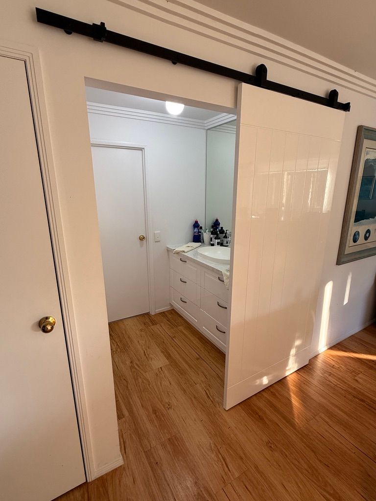 Open Closet with A White Dresser and Bottles Viewed Through a Sliding Barn Door — JPR Concepts in Burleigh Heads, QLD