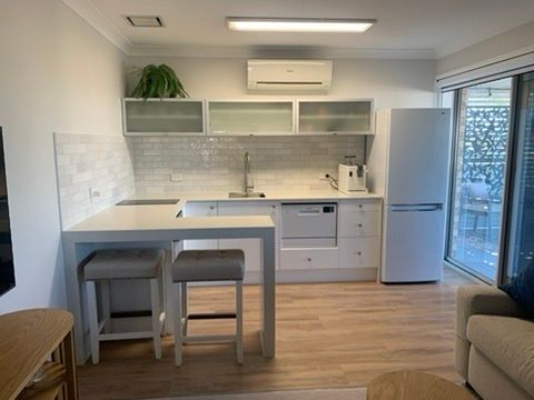 Modern White Kitchen and Dining Area with Island and A Couch by The Window — JPR Concepts in Burleigh Heads, QLD
